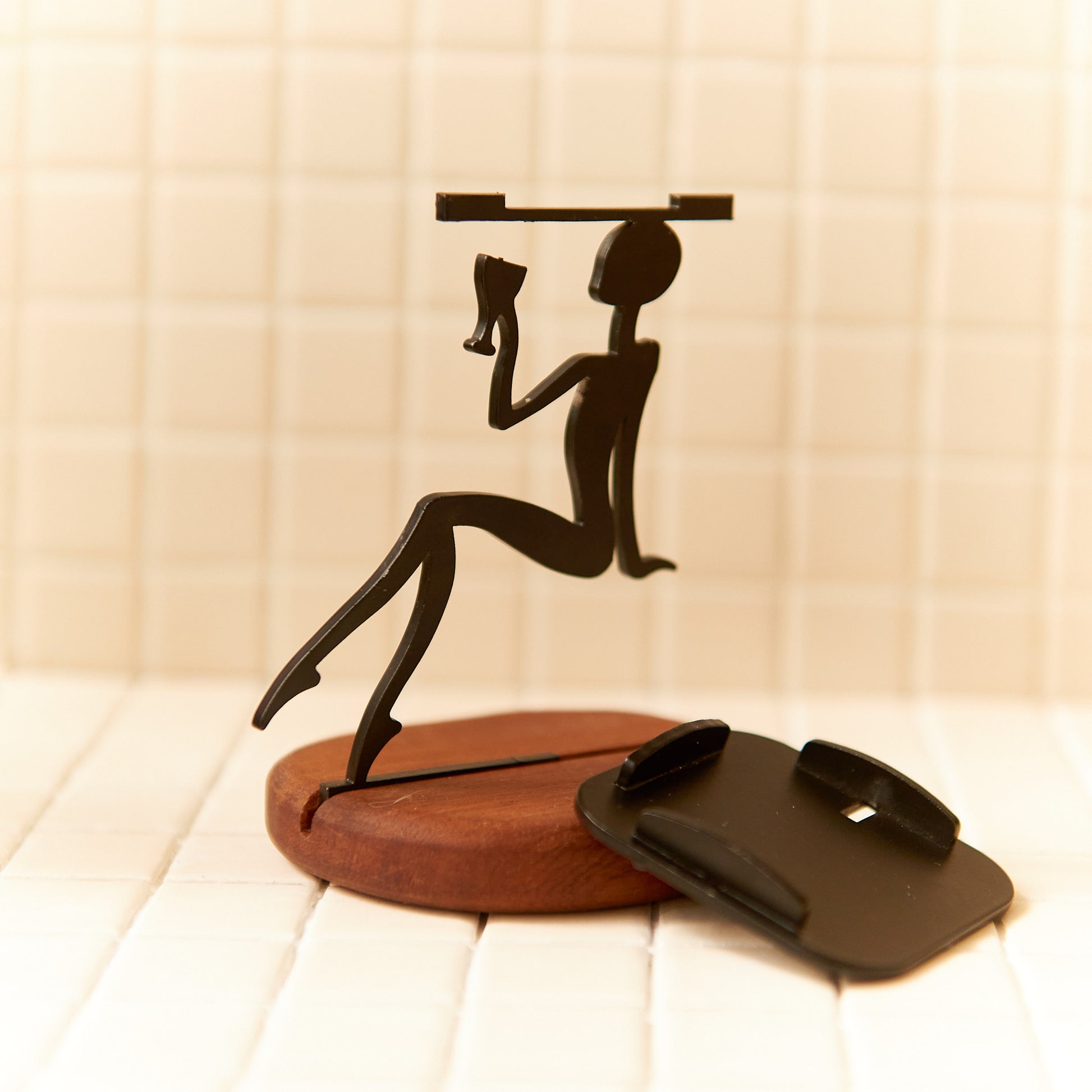 Minimalist alien figurine holding a wine glass, crafted in matte black metal on a round wooden base — handmade by Zeugman.