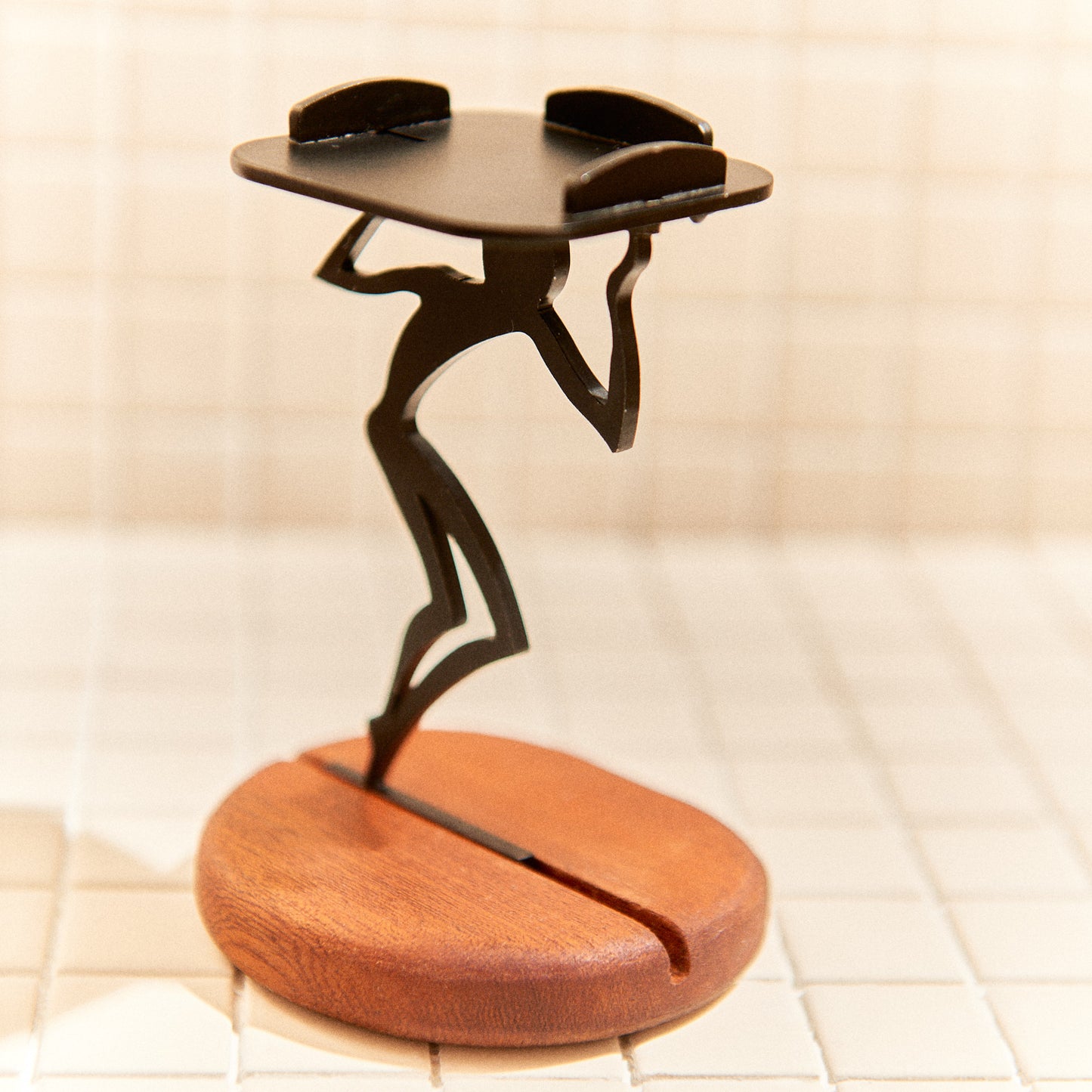 Metal figurine balancing a candle holder on mahogany base, symbolizing cosmic burden.